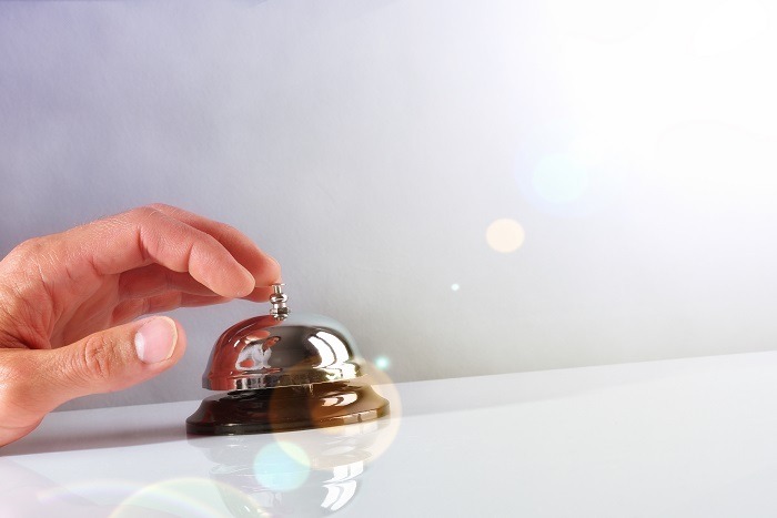Hand of a Customer ringing the bell hotel service on a table white glass. Concept hotel, travel, room. Front view