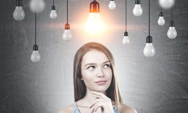 Portrait of a young woman with long fair hair wearing a blue dress and thinking. A blackboard background with many lightbulbs. One is lit.